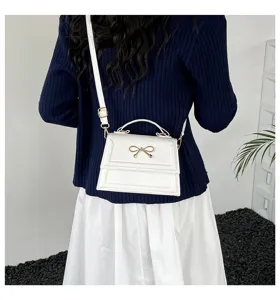 Vue détaillée de l'élégant sac bandoulière blanc avec un joli nœud doré comme accessoire chic.