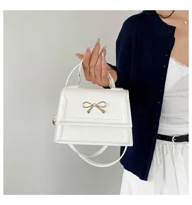 Élégant petit sac à bandoulière blanc pour femme avec un délicat détail de nœud doré.