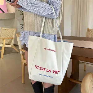 Close-up of white canvas tote bag with embroidered red C'EST LA VIE lettering.