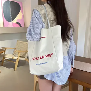 Casual commuter white canvas tote bag with embroidered letter details shown on model