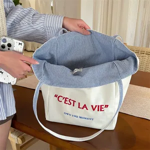 Detail view of canvas tote bag showing striped lining and C'est La Vie embroidery