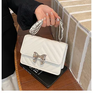 Close-up detail of a white quilted crossbody handbag with a stylish silver bow and chain handle.