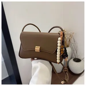 Dettaglio della borsa a tracolla marrone con perline di legno e chiusura metallica curata.