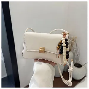 Borsa a tracolla bianca minimalista chic con cinturino annodato e ciondolo in perline di legno.