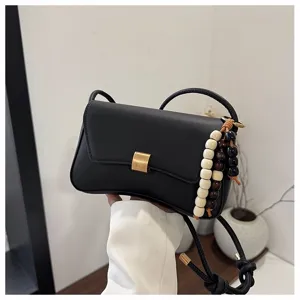 Primo piano di borsa a tracolla nera con base curva, chiusura dorata e ciondolo di perle.