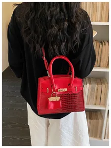 Detailed view of a fashionable red crocodile-embossed shoulder bag with metal lock charm.
