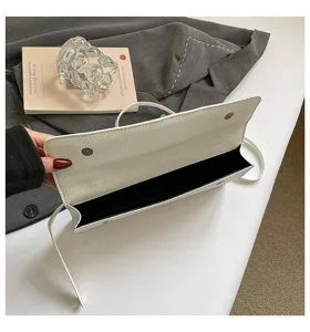 Detalle de bolso de mano de cuero blanco con cierre magnético y diseño elegante.
