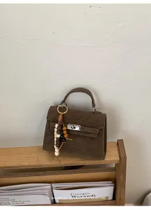 Gros plan sur le sac à main en daim marron avec fermoir métallique et breloque en perles.