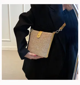 Woven straw crossbody bag detail showing texture, yellow leather trim and snap button.