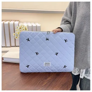 Vista detallada de funda acolchada azul claro para portátil con bonitos lazos bordados.