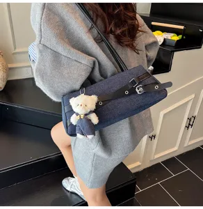 Detail view of a dark denim shoulder underarm bag with black belt and cute bear pendant.