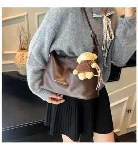Detail view of the brown leather hobo shoulder bag featuring a cute bear pendant and metal tag.