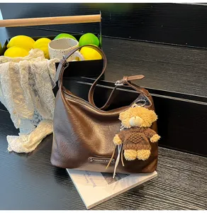 Stylish brown PU leather underarm shoulder bag with cute knitted bear pendant for women.