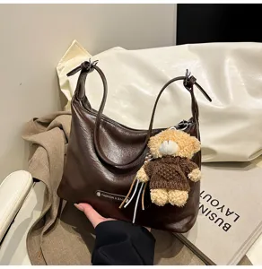Detailed view of the brown leather shoulder bag with cute bear keychain accessory.