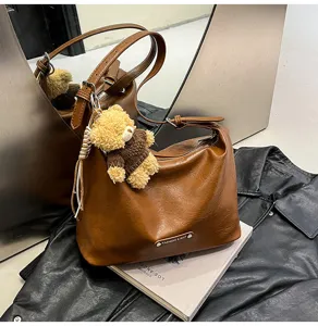 Stylish brown shoulder hobo bag with cute plush bear pendant, trendy autumn design for women.