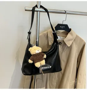 Black leather hobo shoulder bag detail featuring cute bear plush pendant and metal hardware accent.