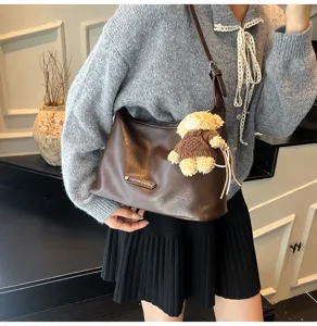 Dark brown leather underarm shoulder bag with cute knit bear pendant, stylish women daily use.
