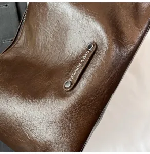 Close-up detail of a dark brown faux leather underarm bag featuring a stylish metal rivet tag.