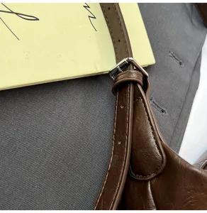 Close-up detail of brown leather shoulder bag strap with adjustable metal buckle craftsmanship.