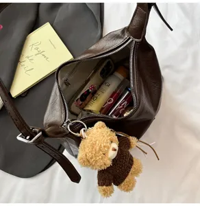 Detailed view of a stylish dark brown leather underarm bag featuring a cute plush bear keychain.
