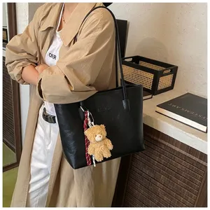 Detail view of black PU leather tote bag featuring cute teddy bear pendant and commuter style.
