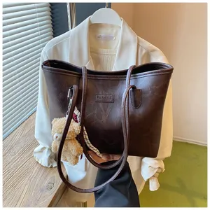 Detail view of brown PU leather tote bag with shoulder straps and cute bear pendant.