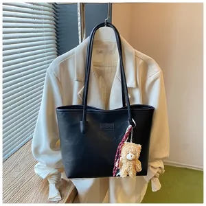 Black PU leather tote bag detail view, large capacity shoulder bag with cute bear pendant.