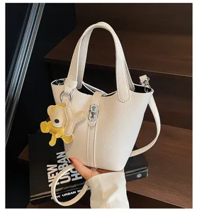 Bolso cubo de cuero blanco con patrón litchi, cierre de cerradura y lindo colgante de oso.