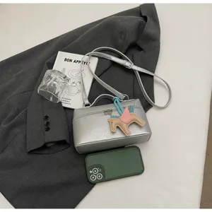Bolso cruzado tipo caja metalizada plateada detalle con dije de caballo alado.