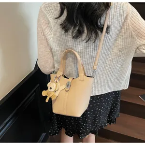 Vista detallada de un bolso de mano estilo cubo minimalista con textura litchi y un osito.