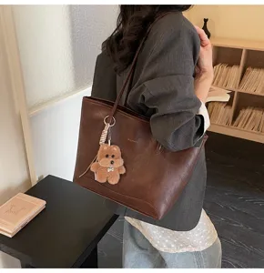 Vista detallada del bolso tote de piel PU marrón con bonito colgante de oso y correa.