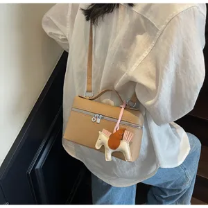 Vista detallada del elegante bolso marrón de cuero con colgante de caballo y cremallera.