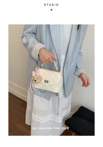 Closeup view of stylish white quilted chain crossbody bag featuring adorable bear charm accent.