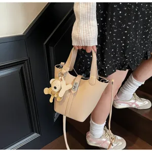 Vista detallada del bolso cubo beige con patrón de lichi y colgante de oso para mujeres.