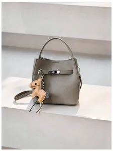 Graue Eimer Handtasche aus Narbenleder mit Henkel und süßem Pferdeanhänger Detail.