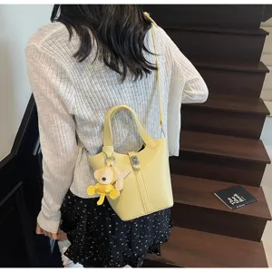 Detalle de bolso cubo amarillo, estilo cruzado casual con lindo colgante de mono y asa práctica.