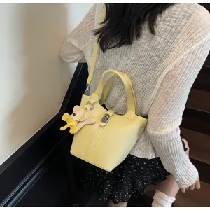 Detalle del bolso cubo amarillo con textura litchi, elegante bolso casual con osito y candado.