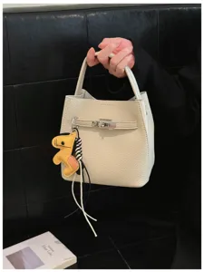 Detailaufnahme einer cremefarbenen Lederbeuteltasche mit Metallverschluss und Pferdeanhänger.
