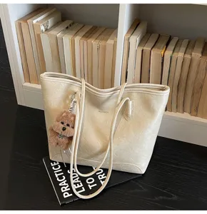 Vista detallada del bolso tote beige casual con llavero de oso frente a la estantería.