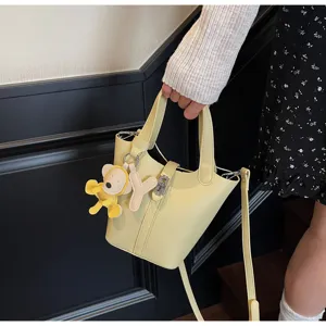 Vista detallada de un elegante bolso cubo amarillo con colgante de oso y correa.