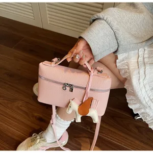 Detalle de bolso de mano tipo caja en cuero PU texturado rosa con dije de caballo alado.
