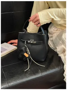 Detailansicht der schwarzen Eimer Tasche mit Metallverschluss und niedlichem Anhänger.