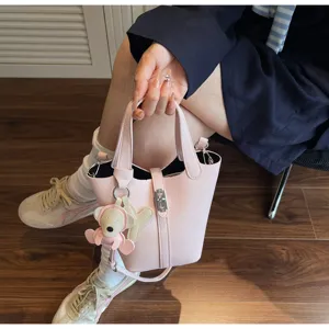 Vista detallada del bolso cubo rosa con patrón de lichi, cierre central y dije de osito tierno.