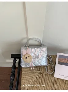 Silver quilted shoulder bag with chic chain strap and cute teddy bear keychain detail.