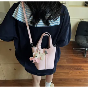 Detalle de bolso tipo cubo de cuero con patrón de lichi rosa con correa y dije lindo.