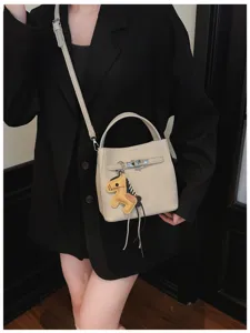 Schicke beige Eimer Tasche mit Metallverschluss und Pferd Anhänger für elegante Frauen.