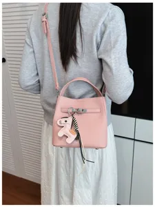 Detailansicht der rosa Lychee-Muster Eimer Tasche mit Schloss-Dekor und Pferd-Anhänger am Model.