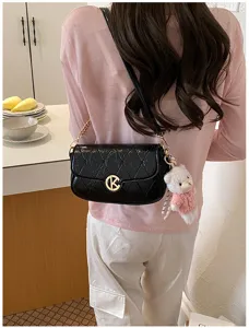 Bolso de hombro acolchado negro con cierre K dorado y adorable colgante de peluche de osito.