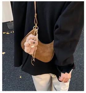 Stylish brown suede crescent shoulder bag with cute plush puppy pendant detail for women.