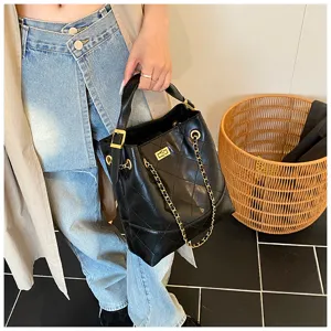 Bolso cubo acolchado negro con correa de cadena dorada y cierre de giro elegante.